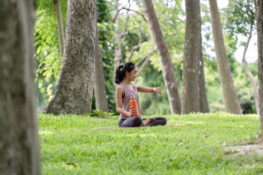 Young Woman Relaxing and Practicing Yoga Outdoors in a Serene Park Setting Surrounded by Trees and Nature photo