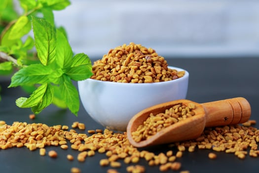 Fenugreek seeds in a bowl on a blue background with green leaves photo