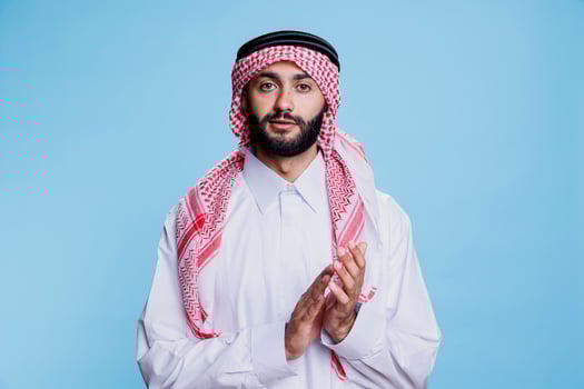 Muslim man in thobe and ghutra applauding with hands, showing support and approval studio portrait. Arab person wearing traditional outfit clapping arms and looking at camera photo
