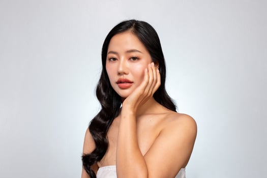 An elegant Asian woman poses with her hand on her chin against a grey background. photo