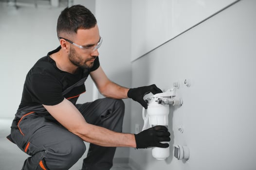 Young man in workwear using pliers while installing water filtration system photo
