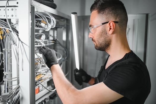 A technician works with server equipment in a data center. A man commutes wires in a server room photo
