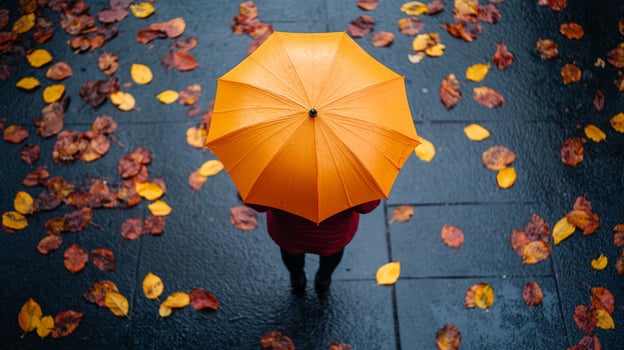 Top view of person under a yellow umbrella held by hands, with autumn fallen leaves on the sidewalk photo