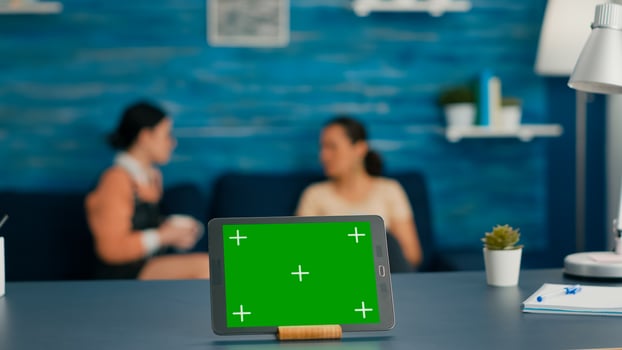 Isolated digital tablet with mock up green screen chroma key display standing on office desk in living room. In background room collegues talking about online communication photo
