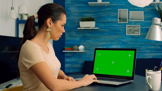 Caucasian female typing on laptop computer with mock up green screen chroma key display for online communication sitting on desk table. Freelancer working with isolated pc in home office studio photo