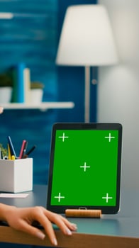 Freelancer woman holding cup of coffee looking at tablet computer with mock up green screen chroma key sitting on desk table. Caucasian female browsing on isolated device from home office room photo