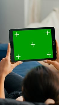 Woman sitting on sofa in living room watching movies on tablet computer with mock up green screen chroma key display. Freelancer using isolated touchscreen device for social networks browsing photo