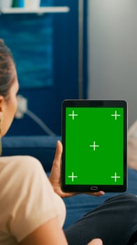 Business woman looking at tablet computer with mock up green screen chroma key display sitting on sofa in living room. Freelancer using isolated touchscreen device for social networks browsing photo
