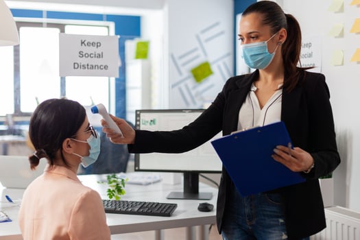Entrepreneur womanchecking colleague body temperature using digital thermomter with infrared as safety precatuon during global pandemic with coronavirus. Woman wearing face mask to prevent virus infection. photo
