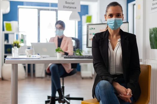 Entreprene portrait looking at camera with face mask as safety precaution keepig social distancing from coworkes during clobal outbreak with covid-19. Business employee working behind separation plastic board. photo