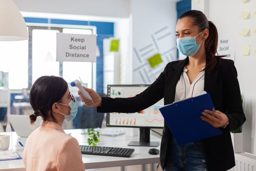 Company worker keeping social distancing scanning colleague temperature with infrared themermoter to prevent infection with virus during global pandemic with covid-19. Checking healthcare of office worker for fever. photo