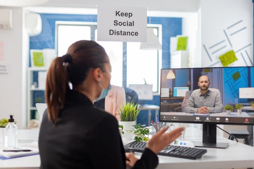 Back shot of businesswoman wearing medical face mask talking on videocall meeting with remotely team. Executive freelancer working in new normal company office during coronavirus pandemic. photo