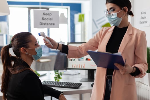 Businesswoman measuring temperature using infrared thermometer to prevent infection with coronavirus. Manager with medical face mask against covid19 working in business office during virus pandemic photo