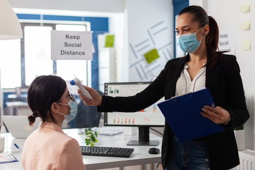 Businesswoman using medical thermometer monitoring collegue temperature to prevent infection with coronavirus during global pandemic in startup business office. Teamwork with face mask against covid19 photo