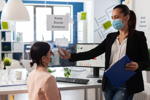 Manager using medical thermometer checking collegue temperature to prevent infection with coronavirus during global pandemic in startup business office. Teamwork with face mask against covid19 photo