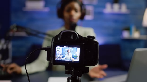 African influencer recording blog looking at professional camera at online talk show home studio. Social media content creator streaming online broadcast, blogger discussing wearing headphones. photo