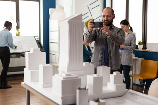 Architect profession man looking at maquette layout using smartphone to design building model plan maquette. Urban designer constructor working on professional modern construction photo