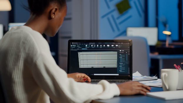 Black freelancer architect working in 3D software to elaborate container design sitting at desk in business office at midnight. Focused engineer creating and studying prototype, analysing scale model photo
