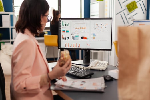 Businesswoman eating tasty sandwich having meal break working in business company office during takeout lunchbreak. Fast food order paper bag delivered at workplace. Woman typing strategy on computer. photo