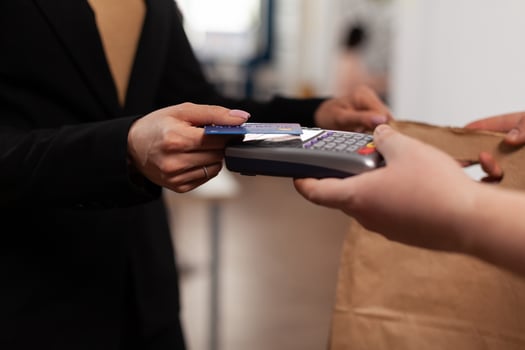 Close up of business woman holding credit card of pos, using contactless technology. Customer paying for their order with a credit card. Holding takeaway food in paper bag. photo