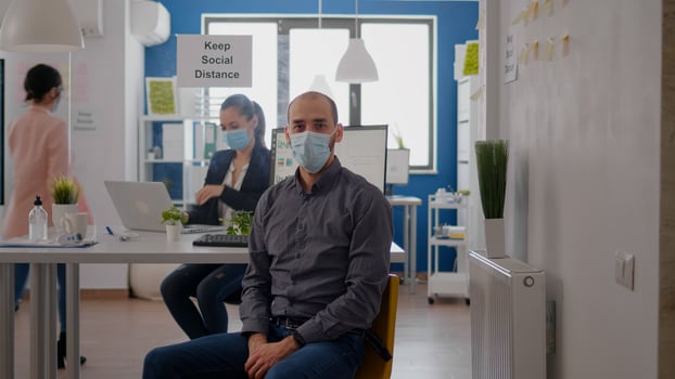 Portrait of entrepreneur man wearing protective face mask against coronavirus pandemic. Employee working at table desk in business office maintain social distancing to prevent virus illness photo