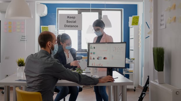 Teamworkers wearing protective medical face mask working at marketing project analysing reports while maintain social distancing in new normal office during covid19 global pandemic photo