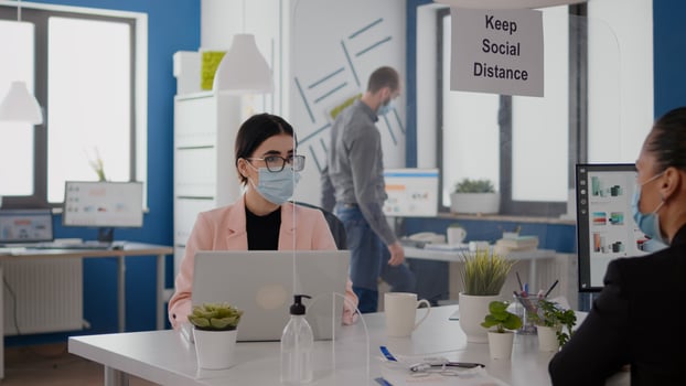 Business team with face masks planning marketing project while looking into monitor for statistics sitting in new normal office. Coworkers respecting social distancing during coronavirus global pandemic photo