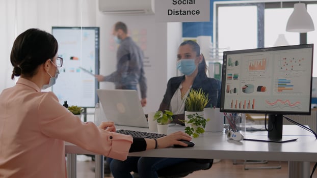 Company team looking at financial graphics while working on computer in business office, wearing protective face mask to avoid infection with covid19. Team respecting social distancing photo