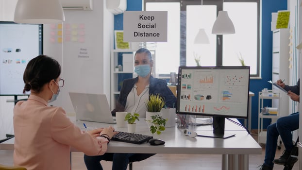 Business team typing financial strategy on laptop, wearing face mask to prevent infection with covid19 while sitting at office desk. Coworkers keeping social distancing to avoid virus disease photo