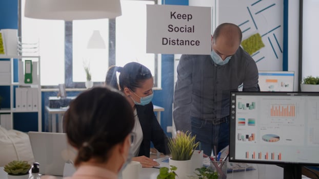 Business people with medical face masks sitting in new normal company office analysing financial project during covid19 pandemic. Coworkers keeping social distancing to avoid virus disease photo