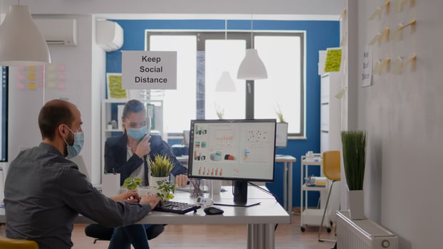 Freelancer with protection medical face mask working on laptop computer while talking on phone with team. Businesswoman sitting at desk table in new normal company office during covid19 quarantine photo