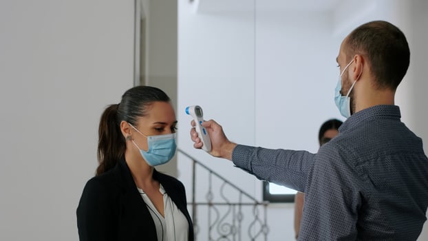 Freelancer with protection face mask measure temperature with thermometer before coworkers enter in business office. Collegues respecting social distance to avoid infection with covid19 photo
