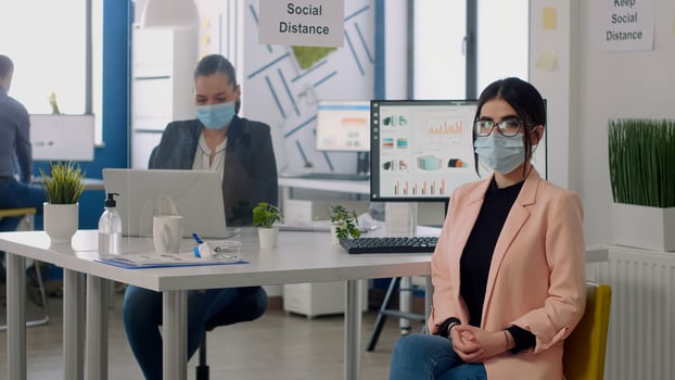 Portrait of manager with face mask sitting on chair at desk table in nre normal business company office. Teamworkers working in background respecting social distancing during coronavirus pandemic photo