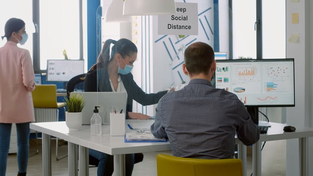 Teamworkers wearing face masks while working at marketing project using computer sitting at table desk in business company office. Coworkers keeping social distancing to avoid infection with covid19 photo