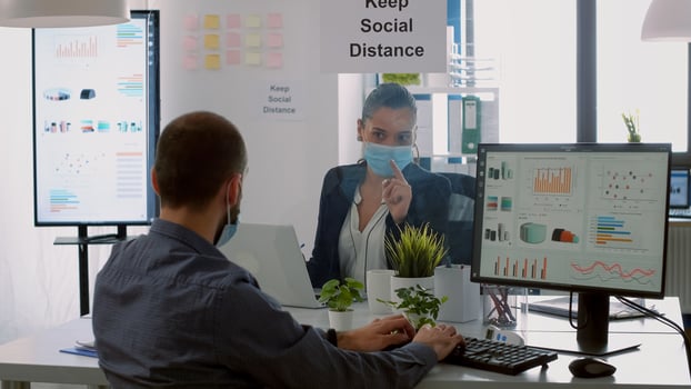 Business team with protection face masks working together in company office during corona virus global pandemic. Coworkers keeping social distancing while typing on computer checking reports photo