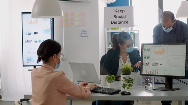 Group of business people with face masks working in new normal company office analysing financial project during coronavirus global pandemic. Coworkers keeping social distancing to avoid virus disease photo