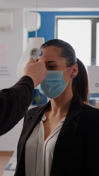 Business man with protective face mask checking collegues temperature using infrared thermometer to prevent virus infection. Coworkers keeping social distance to prevent coronavirus spread photo