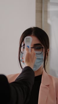 Close up of woman measuring temperature with medical thermometer to prevent covid 19. Coworkers keeping social distance wearing protection face mask at work place during coronavirus global pandemic photo