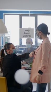 Two coworkers touching elbow during coronavirus global pandemic while working at business project wearing medical face mask to prevent infection with virus disease. Company mantain social distancing photo