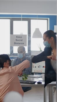 Coworkers touching elbow to avoid infection with coronavirus, business team wearing medical face mask while sitting on table desk working on company project respecting social distance photo