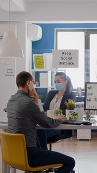 Businessman with protective face mask talking on phone organizing businees meeting. Coworkers respecting social distancing while working at company office during coronavirus global pandemic photo