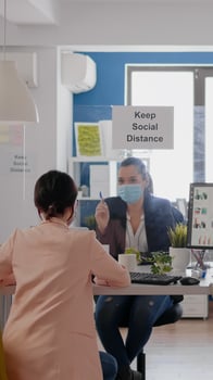 Business womens with medical face masks talking about management statistics working at desk table in new normal company office. Team mantain social distancing to avoid infection with coronavirus photo