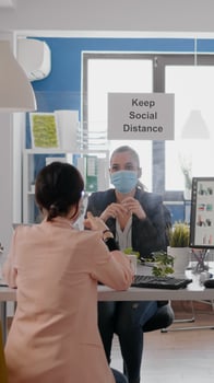 Coworkers working at business meeting wearing protective face mask respecting social distancing to avoid covid19 infection, while sitting at table desk in start up office company. photo