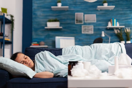 Woman feeling sick sleeping at home on the couch, recovering after cold and flu symptoms. Having fever and taking medicine treatment while resting in bedroom after seasonal disease photo