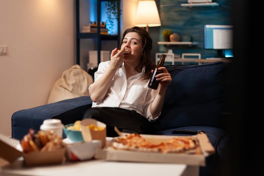 Happy woman eating tasty delicious delivery pizza slice relaxing on sofa watching comedy movie on television in living room. Caucasian female enjoying takeaway fast home delivered in evening photo