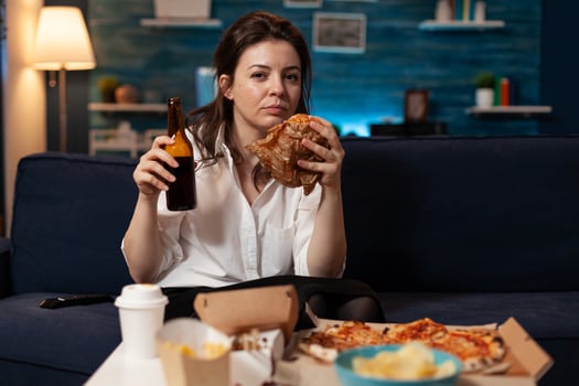 Portrait of caucasian woman looking into camera relaxing on sofa in living room enjoying takeaway food home delivery. Woman eating tasty delicious burger. Fastfood lunch meal order photo