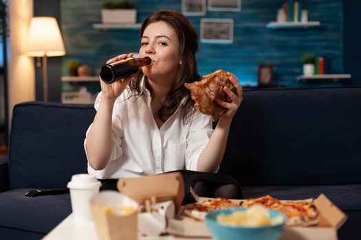 Portrait of woman looking into camera during fastfood lunch meal order relaxing on sofa late at night in living room. Caucasian female enjoying tasty burger, takeaway food home delivered photo