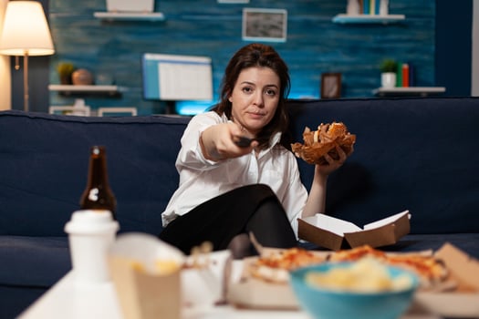 Portrait of woman changing channels using remote watching entertainment movie series sitting on sofa in living room late at night. Caucasian female enjoying takeaway food home delivered photo