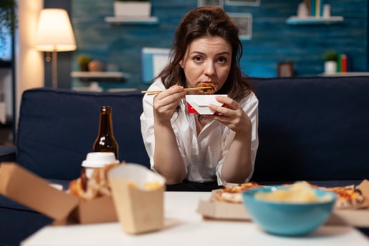 Portrait of caucasian female looking into camera while eating chinese chopstick relaxing on sofa in living room late at night. Woman enjoying takeaway food home delivered. Tasty fastfood lunch order photo