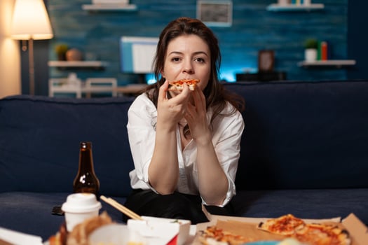 Portrait of caucasian female sitting on sofa eating slice of pizza enjoying takeaway food home delivered in living room. Woman relaxing in living room ordering tasty delicious meal lunch. photo